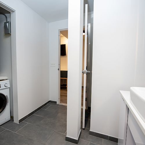 The image shows a laundry room with a washing machine, utility area, sink, and two adjacent doors leading to other rooms.