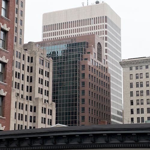 The image shows a cityscape featuring several tall buildings, including a variety of architectural styles and window designs, under an overcast sky.